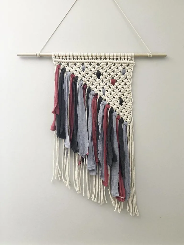 Macrame wall hanging tied with square knots in a triangle pattern with pink, charcoal, and denim blue t-shirt fringe