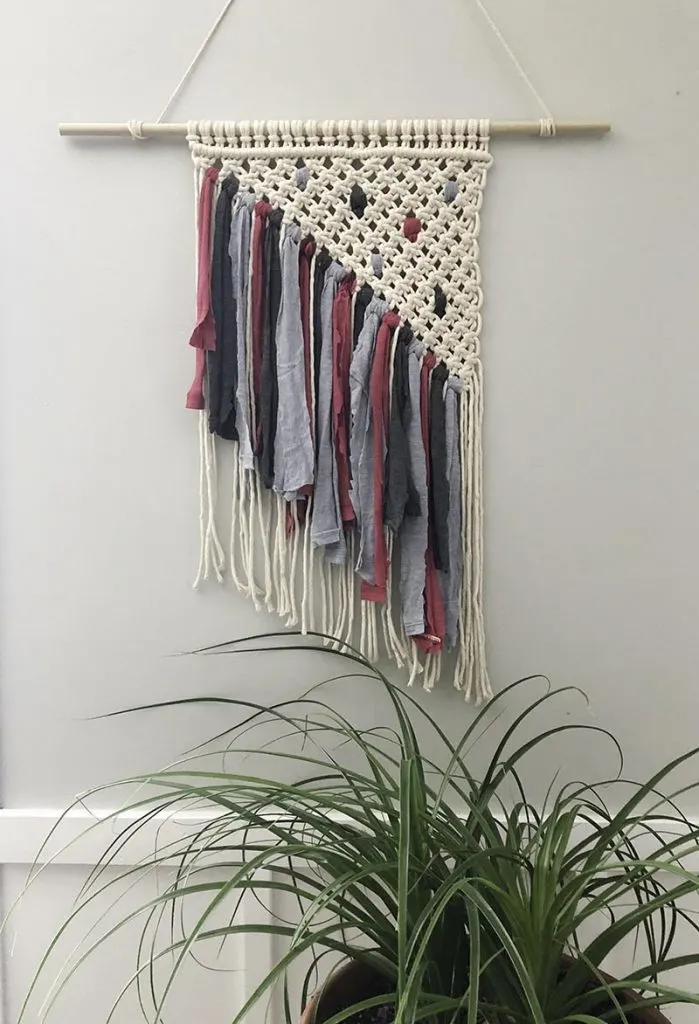 Macrame wall hanging tied with square knots in a triangle pattern with pink, charcoal, and denim blue t-shirt fringe