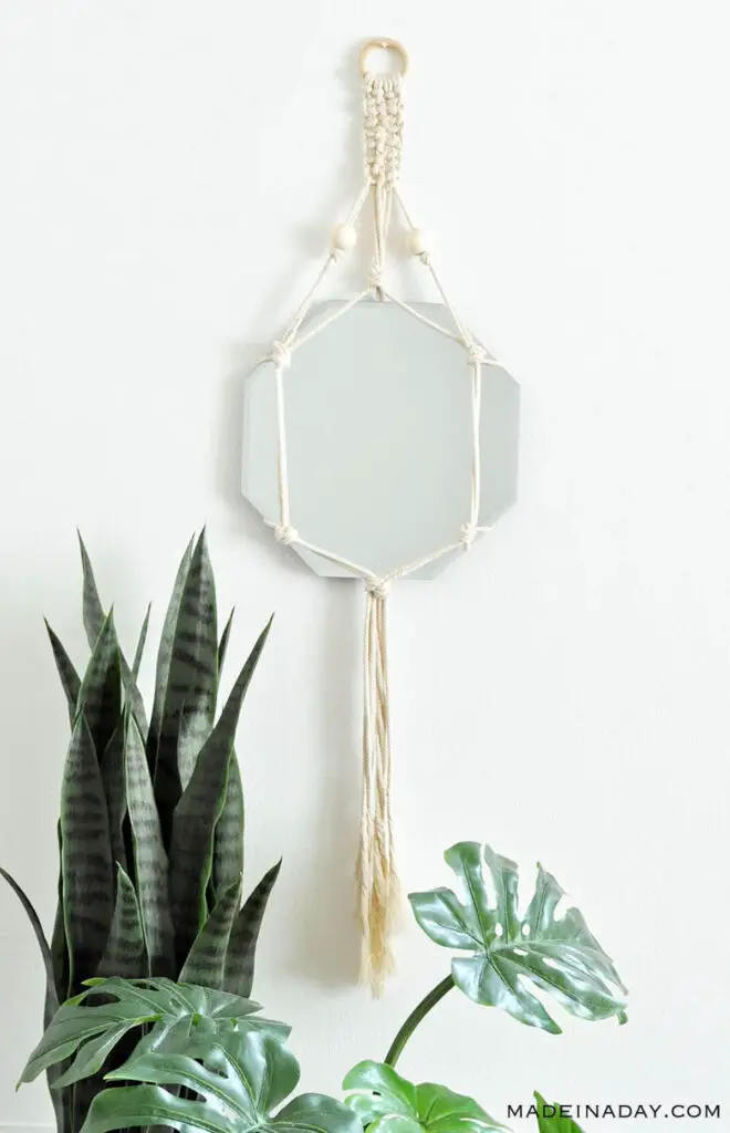 macrame mirror wall hanging on the wall above plants